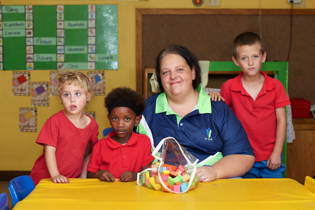 Child in green shirt paints with teacher in white classroom