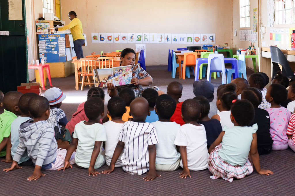 Toddlers in green shirts play in white pre-school with navy-clad teacher